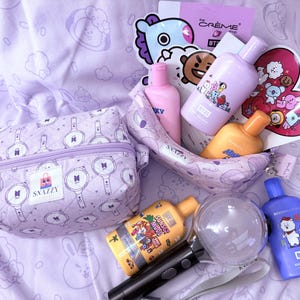 May include: A collection of purple and yellow beauty products and accessories, including bottles, a cosmetic bag, and a light stick. The items are arranged on a lavender patterned surface. The cosmetic bag has a zipper and a logo that says "SNAZZY".