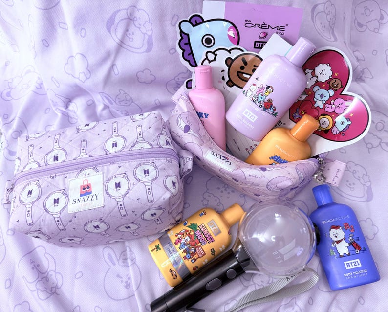 May include: A collection of purple and yellow beauty products and accessories, including bottles, a cosmetic bag, and a light stick. The items are arranged on a lavender patterned surface. The cosmetic bag has a zipper and a logo that says "SNAZZY".