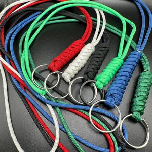 May include: A collection of colorful lanyards with braided accents and metal rings. The lanyards are in various colors, including red, white, black, green, and blue. The metal rings are silver and black.