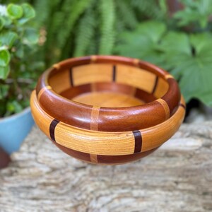 May include: A handcrafted wooden bowl with a multi-toned design. The bowl features alternating bands of light and dark wood, with a rich, natural finish. The interior is a lighter shade of wood, creating a contrast. This decorative bowl is ideal for serving or display.