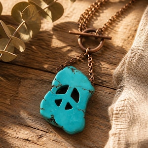 May include: A necklace featuring a bright turquoise stone pendant with a cutout peace sign symbol. The pendant is suspended from a copper-toned metal chain that connects to a circular toggle clasp closure, showcasing a metallic finish.