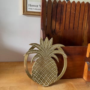 Peut inclure: Un dessous-de-plat doré en forme d'ananas avec un design détaillé. Le dessous-de-plat est entouré d'un cadre circulaire. L'ananas a une surface texturée avec un motif en grille. Le dessous-de-plat est sur une surface en bois.
