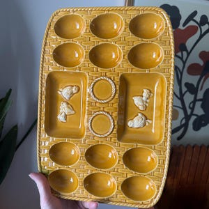Peut inclure: Un plateau de service à œufs vintage en céramique jaune moutarde avec un motif de panier tressé. Le plateau comporte 12 cavités pour les œufs et deux sections rectangulaires avec des motifs de poulet en relief blanc.