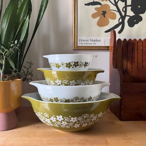 Peut inclure: Un ensemble de quatre bols à mélanger Pyrex vintage de différentes tailles. Les bols présentent un motif floral blanc et vert olive. Le plus grand bol est vert olive avec des fleurs blanches, les plus petits alternent les couleurs.