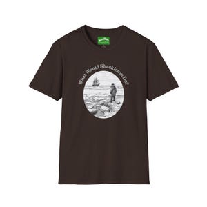 May include: A dark brown t-shirt with a circular graphic. The graphic shows a black and white illustration of a person on a rocky shore, with a ship in the distance. The text "What Would Shackleton Do?" is around the image.