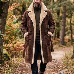 May include: A long brown suede coat with a thick cream-colored shearling lining, a wide notched collar, double-breasted button closures, and a matching waist belt, worn over a dark olive green ribbed turtleneck sweater and dark blue denim jeans.