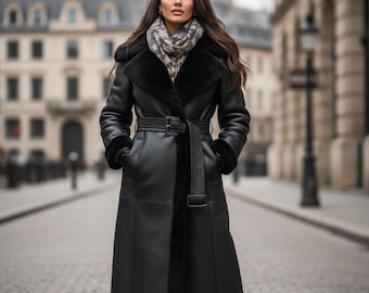 May include: A long, black leather coat with a belted waist and shearling trim. The coat features a wide collar and cuffs, and is worn over a patterned scarf. The coat is knee-length and has a classic, elegant style.