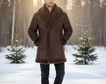 May include: A brown shearling coat with a wide collar and cuffs. The coat has a button-up front and is worn over a dark shirt and black pants. The person is standing in a snowy forest with evergreen trees in the background.