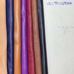 May include: A collection of colorful leather swatches in various shades, including tan, navy blue, orange, purple, burgundy, brown, and black. The word "VELTROSTORE" is written in blue ink on a white background.