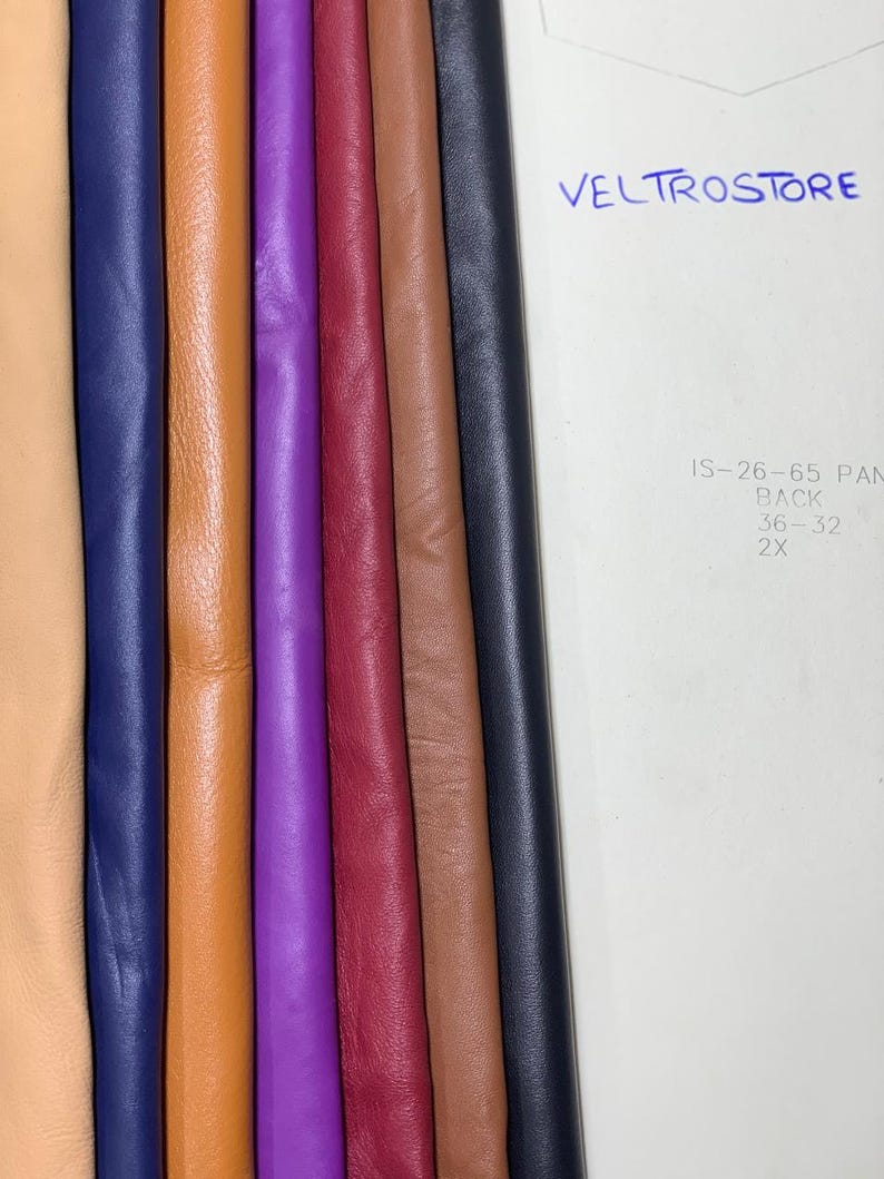 May include: A collection of colorful leather swatches in various shades, including tan, navy blue, orange, purple, burgundy, brown, and black. The word "VELTROSTORE" is written in blue ink on a white background.