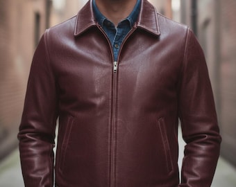 Puede incluir: Chaqueta de cuero burdeos con cremallera y cuello. La chaqueta tiene un cinturón en la cintura y se lleva sobre una camisa vaquera. El color de la chaqueta es un tono profundo y rico de rojo-marrón.