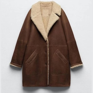 May include: A brown shearling coat with a beige shearling lining and collar. The coat features two front pockets and a button-up closure. The sleeves and collar are trimmed with beige shearling.