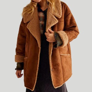 May include: A brown suede-effect coat featuring a tan shearling collar and cuffs. The coat has a classic lapel collar, two front pockets, and a button closure. The interior lining is a lighter tan colour.