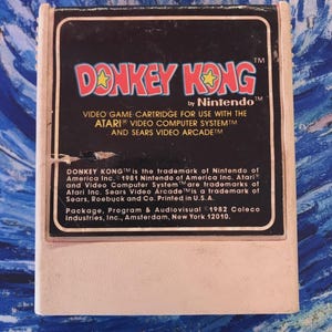 May include: A vintage Donkey Kong video game cartridge by Nintendo. The label features the game title in red and yellow, with the Nintendo logo. The cartridge is designed for use with Atari and Sears video systems. Package, Program & Audiovisual ©1982 Coleco Industries, Inc.