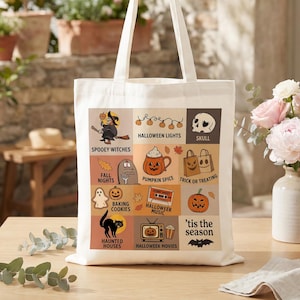 May include: A cream-colored canvas tote bag featuring a grid of twelve colorful Halloween-themed illustrations and text labels including Spooy Witches, Fall Nights, Baking Cookies, Haunted Houses, Halloween Lights, Pumpkin Spice, Halloween Music, and Movies.