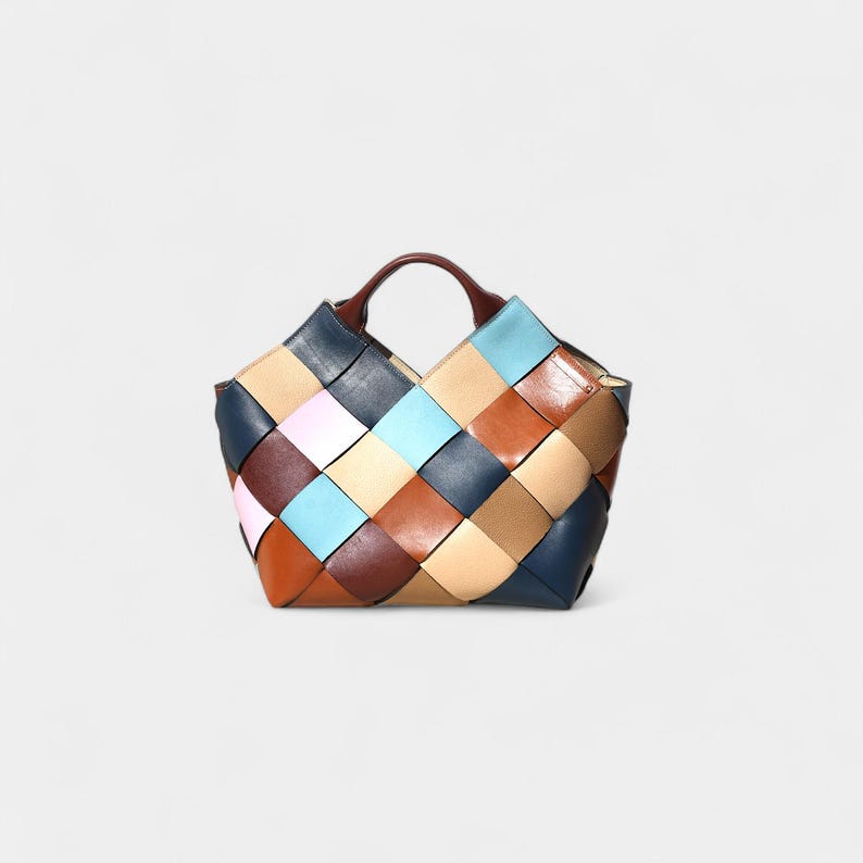 May include: A multi-colored woven leather tote bag. The bag features a patchwork design with squares of various colors, including blue, brown, tan, and pink. It has a brown handle and a structured shape.