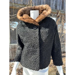 May include: A black vintage jacket with a textured surface and a brown fur collar. The jacket has a single button closure and three-quarter sleeves. The jacket is displayed on a white mannequin.
