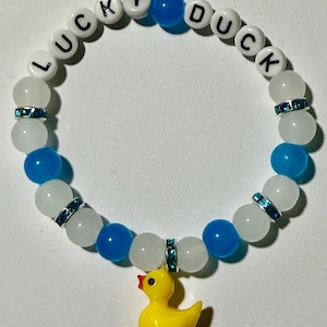 Beaded bracelet featuring blue, white, and crystal-accented beads with white letter beads spelling LUCKY DUCK and a yellow rubber duck pendant.