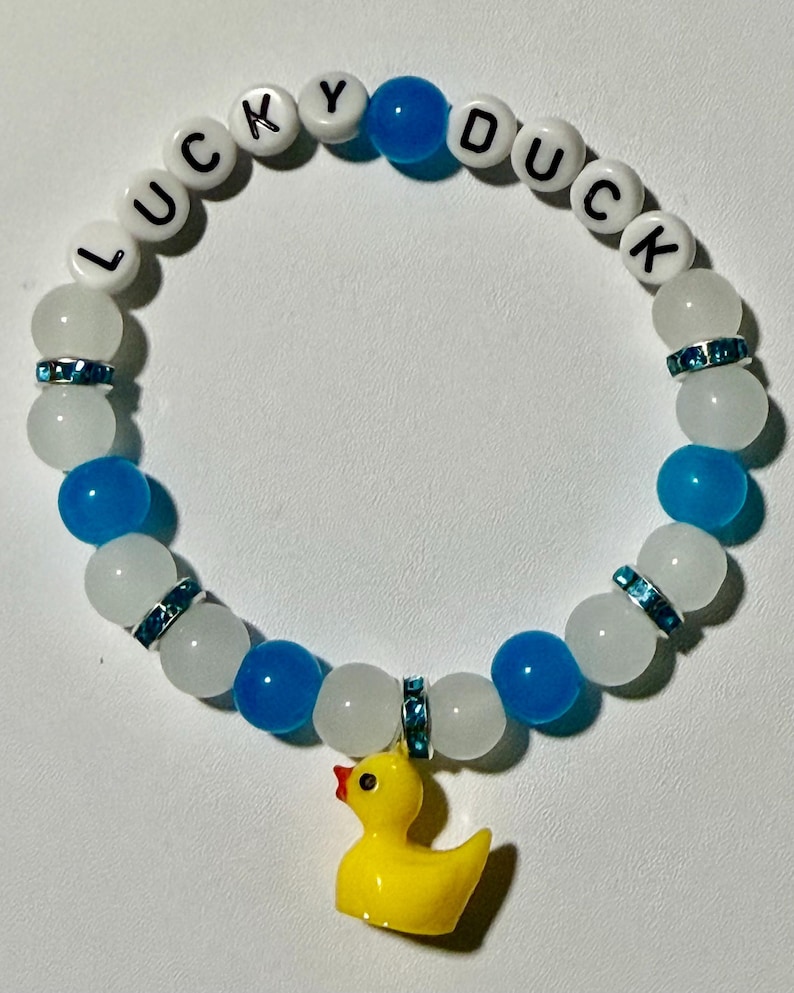 Beaded bracelet featuring blue, white, and crystal-accented beads with white letter beads spelling LUCKY DUCK and a yellow rubber duck pendant.