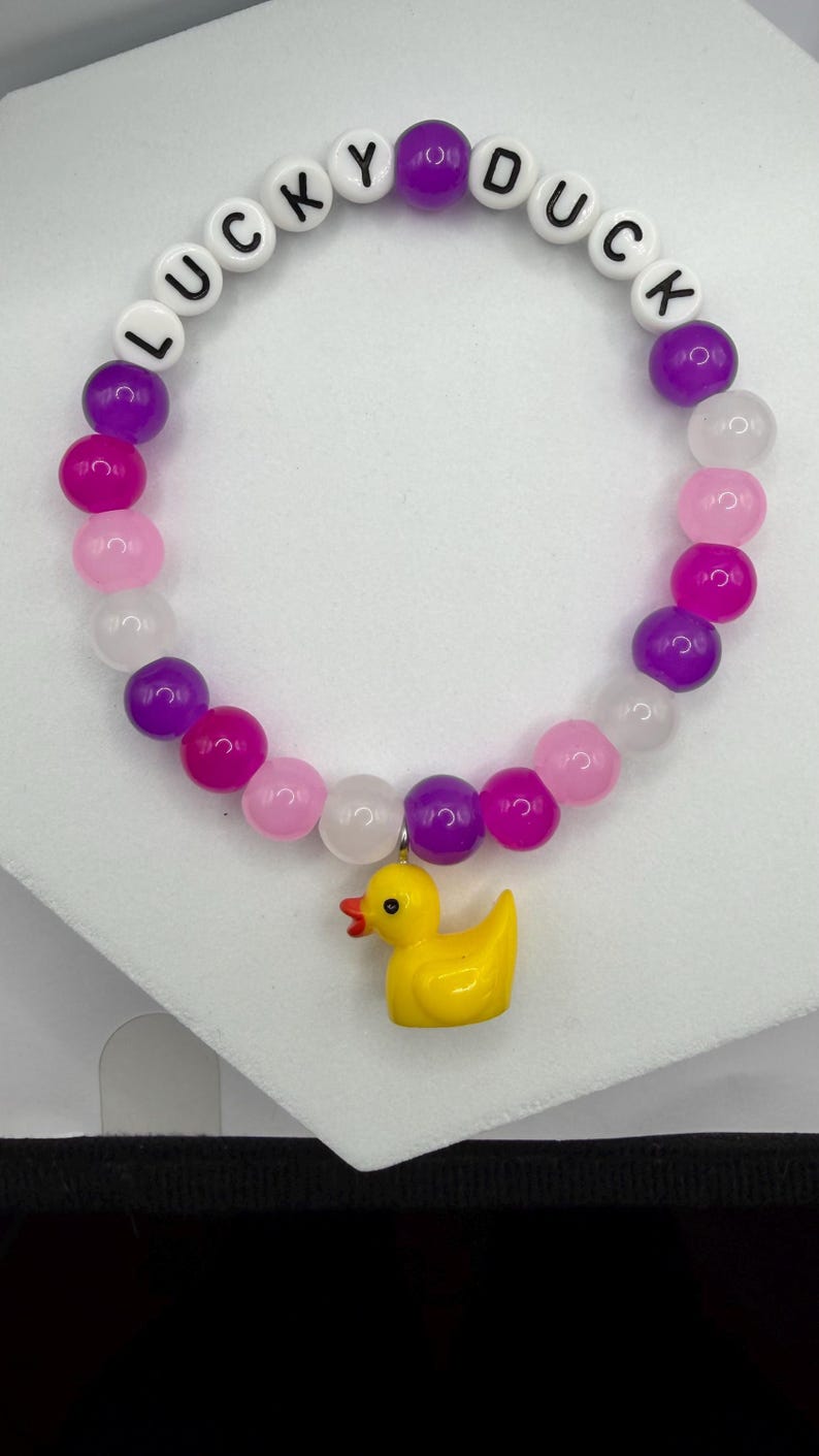 Beaded bracelet with purple and pink stones, white letter beads spelling LUCKY DUCK, and a yellow rubber duck charm.