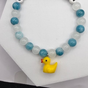 Beaded bracelet with blue and white stones, white letter beads spelling CRUISE FUN, and a yellow rubber duck charm.