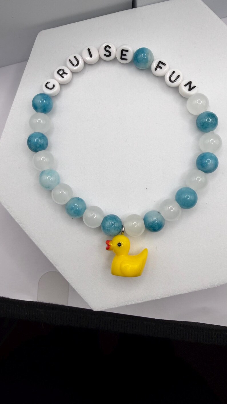 Beaded bracelet with blue and white stones, white letter beads spelling CRUISE FUN, and a yellow rubber duck charm.