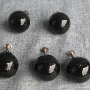 May include: A set of five spherical black cabinet knobs with a glossy finish. Each knob features a smooth, rounded surface and a central metal mounting screw extending from the back, designed for attachment to furniture drawers or cabinet doors.