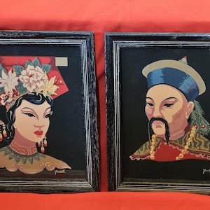 May include: Two framed prints featuring portraits of individuals in traditional attire against a black background. The left print shows a person with a floral headpiece and dangling earrings. The right print depicts a person with a blue hat and mustache.