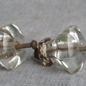 May include: Two clear glass cabinet knobs with a faceted design. Each knob has a metal stem and a decorative base with a mottled brown and white pattern. The knobs are set against a gray background.