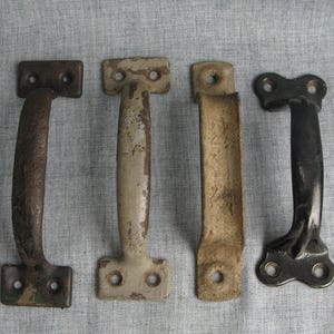 May include: Four vintage metal door pulls in varying colors and styles. The pulls include a dark brown, off-white, tan, and black handle. Each handle has two mounting plates with two holes each for screws.