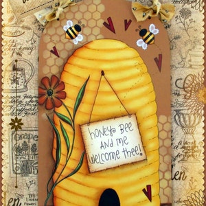 May include: A painted wooden beehive with a sign that reads "honey bee and me welcome thee!"  The beehive is yellow and brown with a honeycomb pattern. There are two bees flying near the top of the beehive. The beehive is surrounded by a brown background with a floral pattern.