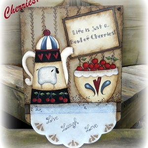 Puede incluir: Un letrero de madera rústico con una tetera pintada, un tazón de cerezas y el texto "Life is just a Bowl of Cherries!" El letrero también tiene un borde festoneado con las palabras "Live, Laugh, Love" pintadas en él.