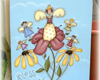 Op de afbeelding: Een blauw geschilderd houten bord met een hart bovenaan en een grillige schildering van engelen en bloemen. Het bord heeft de tekst "Bless My Blooms!"