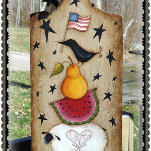 May include: A wooden chopping board with a distressed finish, painted with a black bird, a pear on a watermelon slice, a white sheep with the word "Love" on its side, and stars. The board is tied with a brown ribbon.