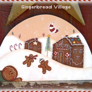 May include: A hand-painted wooden gingerbread village scene with a crescent moon, a star, and a gingerbread house with the word "welcome" on the front. There are three gingerbread people in the snow.