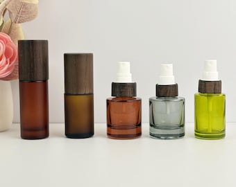 May include: Five glass spray bottles with wooden caps. The bottles are in shades of brown, gray, and green. The two taller bottles have a cylindrical shape, while the others are shorter and square. The spray nozzles are white.