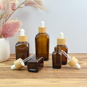 May include: Amber glass dropper bottles with bamboo lids and white droppers. The bottles are in various sizes and shapes, some rectangular and some round. The bottles are arranged on a wooden surface.