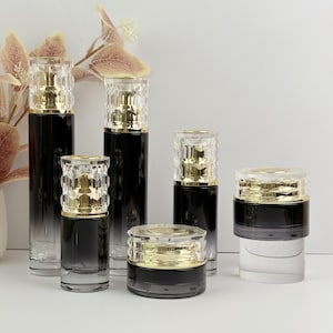May include: An assortment of luxury cosmetic containers. The bottles and jars are black with a gradient effect, topped with gold and clear, faceted lids. The containers vary in size and shape, suggesting a skincare or beauty product line.