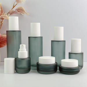 Frosted green glass cosmetic packaging set with various types of bottles and containers, including lotion pump bottles and cream jars, in an organized arrangement.