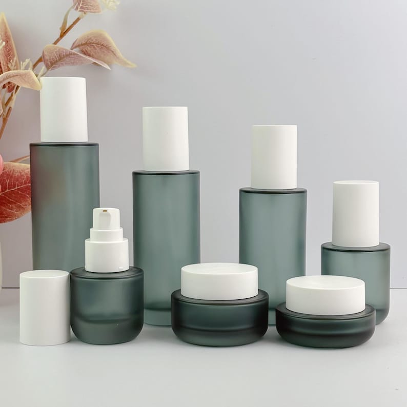Frosted green glass cosmetic packaging set with various types of bottles and containers, including lotion pump bottles and cream jars, in an organized arrangement.