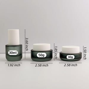 May include: Three cosmetic containers: a 30ml bottle (9.14 cm tall) and two jars, one 50g (4.70 cm) and one 30g (3.81 cm). All have a dark green base and white lids. The jars are 6.55 cm wide.