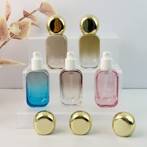 Peut inclure: Plusieurs flacons de parfum en verre avec des bouchons dorés et des vaporisateurs blancs. Les bouteilles sont dans des tons de bleu, de marron et de rose. Les bouchons sont ronds et brillants. Les bouteilles sont exposées sur une plateforme blanche à plusieurs niveaux.