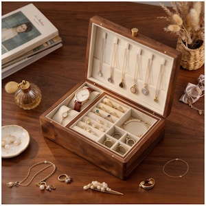 Può includere: Portagioie in legno aperto con più scomparti, tra cui ganci per collane, fessure per anelli e porta orologi. La scatola contiene gioielli in oro, un orologio in pelle marrone e un braccialetto. La scatola è su una superficie di legno.