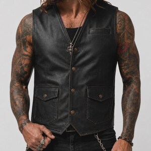 May include: A black leather vest featuring a V-neckline, a front button closure with four metallic buttons, and two lower patch pockets with buttoned flaps. The vest includes a single small welt pocket on the upper left chest area.