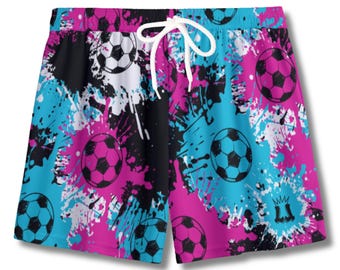 May include: Shorts with a vibrant splash paint design in black, white, turquoise, and pink. The shorts feature a repeating pattern of soccer balls and a white drawstring. The shorts are likely made of a lightweight, breathable material.