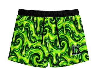 May include: Athletic shorts featuring a vibrant neon green and dark green slime pattern with swirling liquid textures and bubbles. The shorts have a solid black elastic waistband with black drawstring cords and a small black logo with a crown icon.