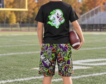 May include: A black short-sleeve t-shirt featuring a graphic of a white ghost holding a brown football on the back, paired with shorts covered in a multi-colored pattern of skulls, footballs, and goalposts. A brown football is held in one hand.