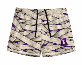 May include: Athletic shorts featuring a graphic print of overlapping beige mummy bandages over a deep purple background. The shorts include a black drawstring at the elastic waistband and a purple logo with a crown icon on the lower right leg.