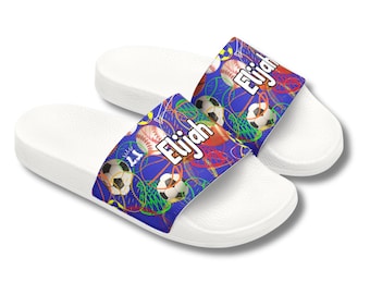 May include: White slide sandals with a blue strap featuring a sports-themed design. The strap displays soccer balls, baseballs, and the name "Elijah" in white. The sandals are designed for casual wear.