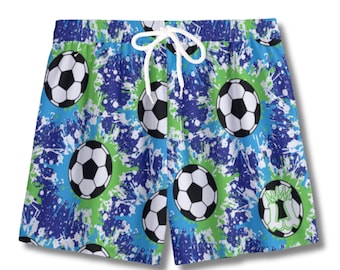May include: Blue and green swim trunks with a soccer ball pattern. The shorts feature a white drawstring and a repeating pattern of black and white soccer balls against a background of blue and green paint splatters.